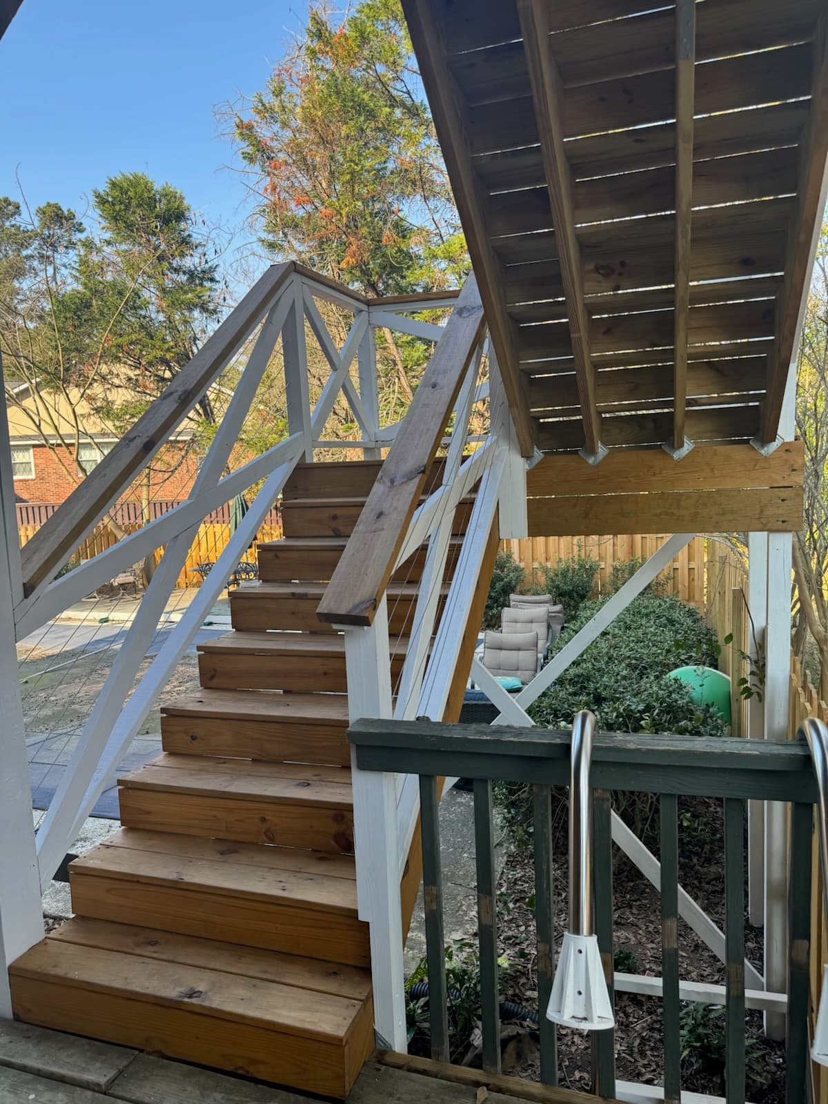 Wooden outdoor stairs with white railings and wire cables lead to a backyard deck.